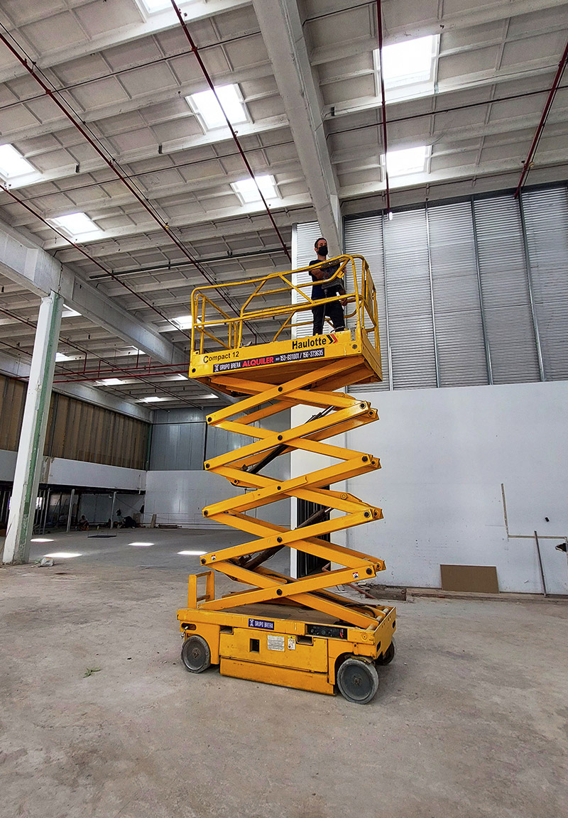 Plataforma de tijera eléctrica trabajando dentro de una nave industrial